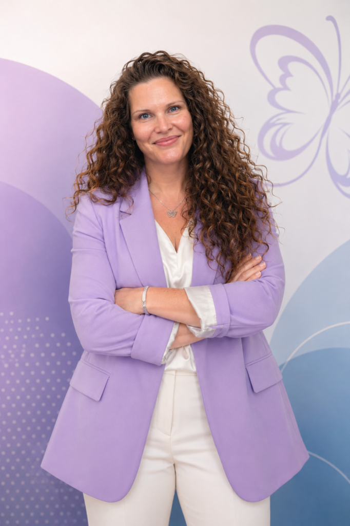 Megan Fuciarelli wearing a lavender blazer with her arms crossed against a light purple background.
